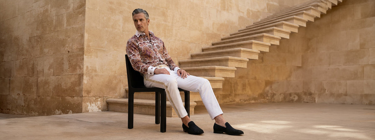 Model in an Angelo Galasso paisley shirt and white trousers seated on stone steps